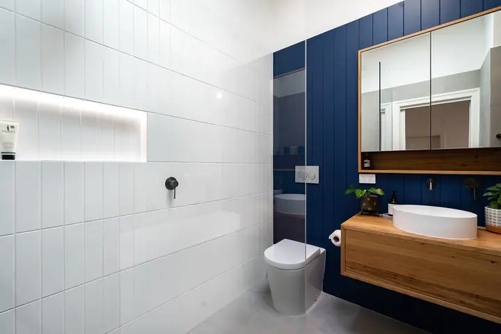 Bathroom with a navy panelled feature wall, timber vanity and wall-hung toilet