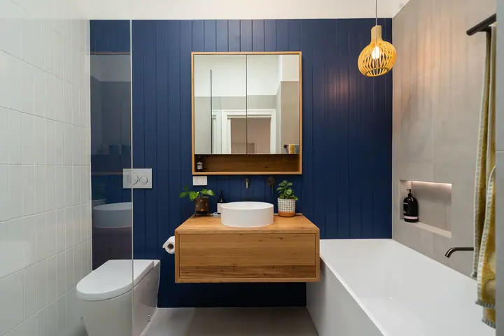 Navy panelled wall with a floating timber vanity, mirror cabinet and bath