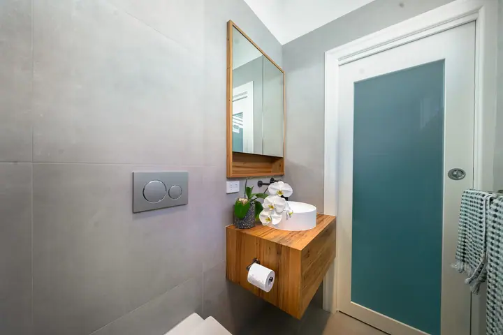 Wall-hung toilet and compact timber vanity beside a frosted door