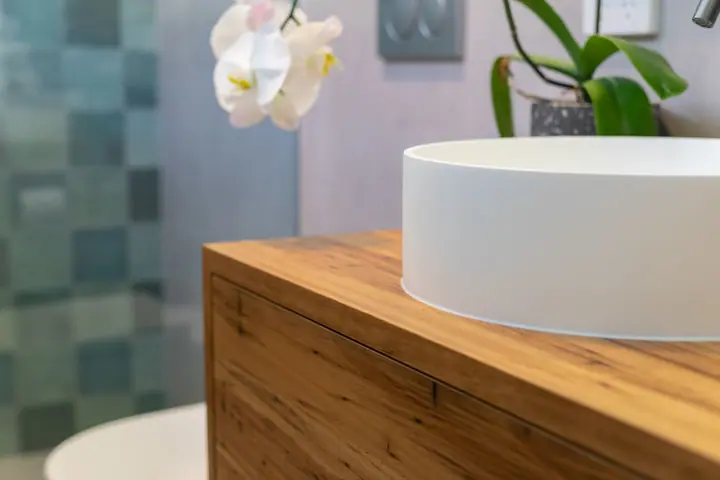 White basin on a timber vanity in front of green tiles