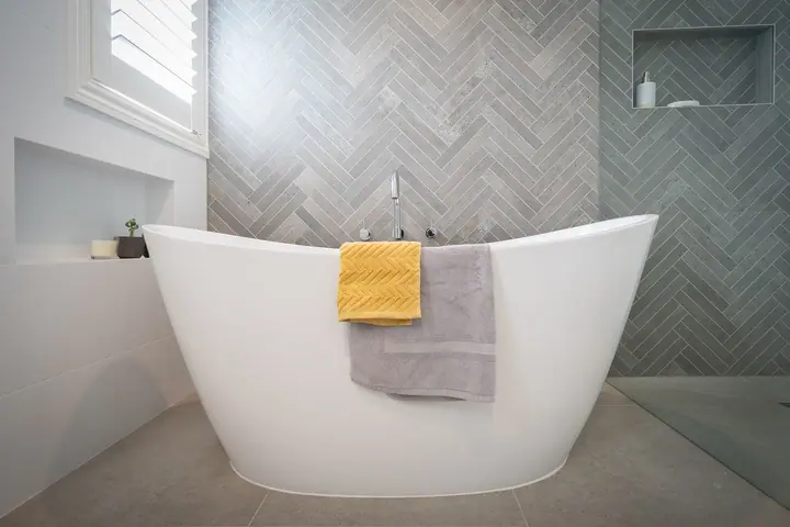 Freestanding bath in front of a grey herringbone feature wall