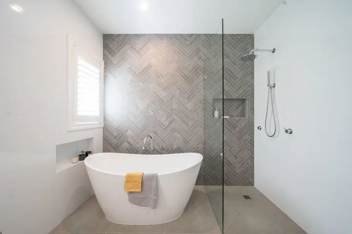 Freestanding bath and frameless glass shower with herringbone tiles