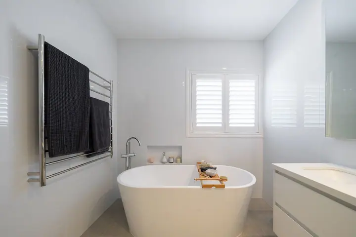 Heated towel rail beside a freestanding bath and white vanity
