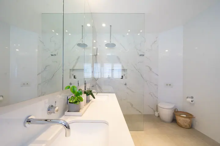 Marble-look tiled bathroom with a double vanity and frameless shower